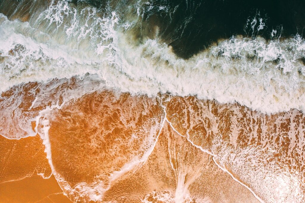 Stunning aerial view of ocean waves crashing on a vibrant sandy beach.
