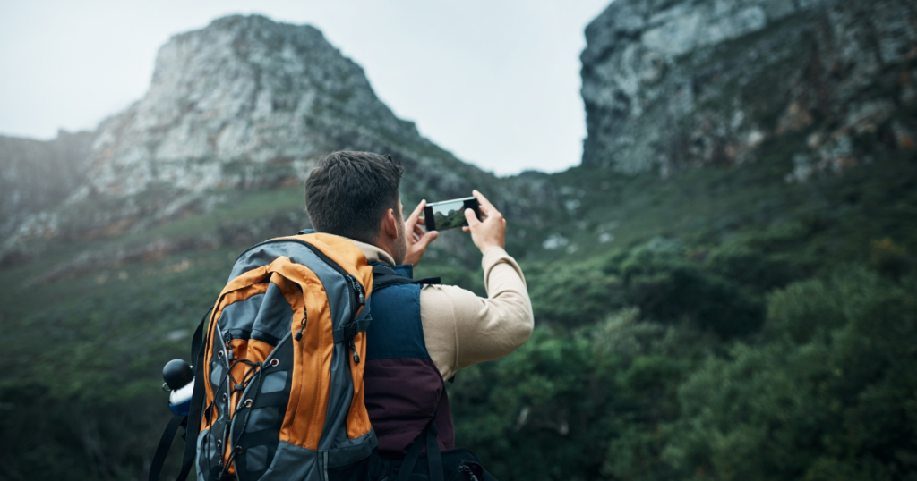 Person hiking and photographing mountains with smartphone.