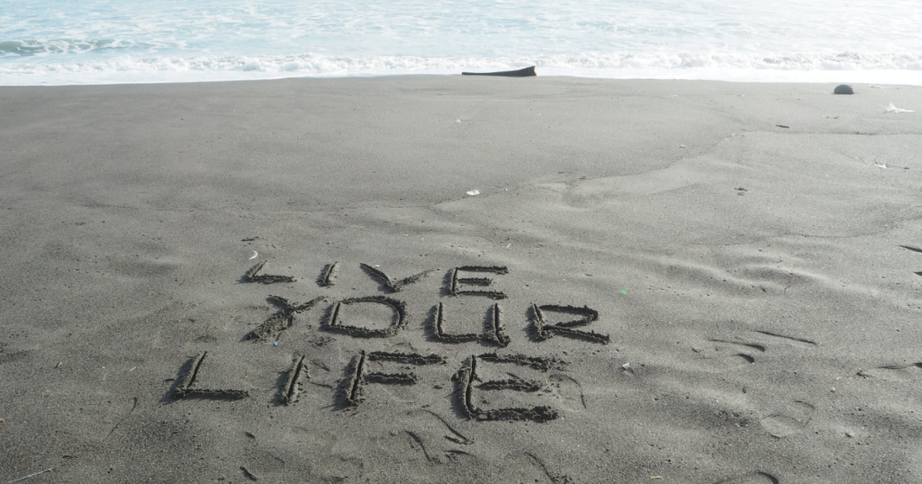 Inspirational phrase 'Live Your Life' on sandy beach.